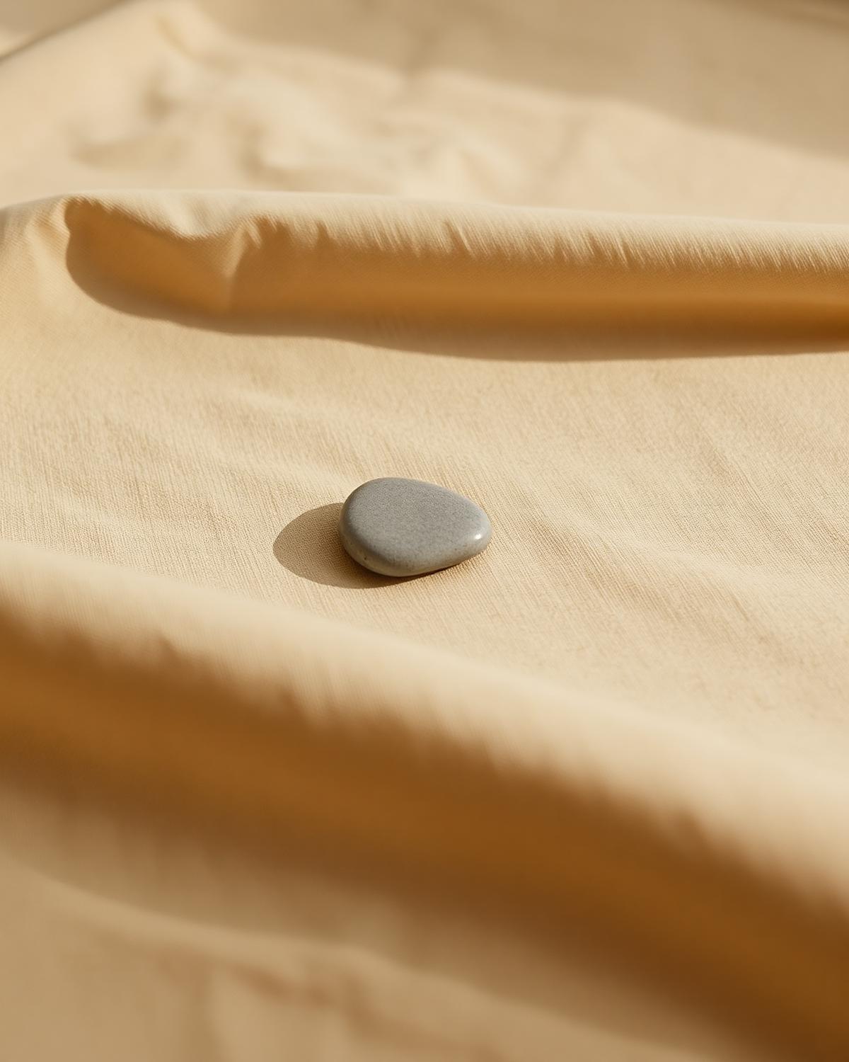 Een kleine kiezel rust op warm beige linnen — stilte en eenvoud.